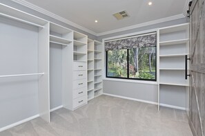 A walk-in closet with open shelving, a large window with a view of trees, and a ceiling vent.
