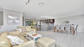 A modern living room with a sofa, coffee table, and dining area with chairs and a table. - Oasis at Salamander Bay (Salamander Bay)