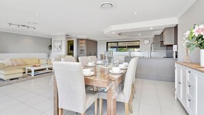 A modern living room with a dining area, a kitchen, and a view of the outdoors. - Oasis at Salamander Bay (Salamander Bay)