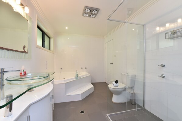 A modern bathroom with a glass-enclosed shower, a glass sink, and a white toilet.