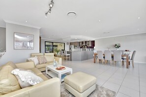 A modern living room with a sofa, coffee table, and ottoman, a dining area with chairs and a table, and a kitchen with a central island.