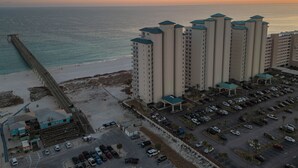 A high-rise hotel with multiple floors, a parking lot, and a beach in the background.