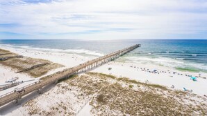 A beach with a long pier extending into the ocean, sandy areas, and a clear sky.