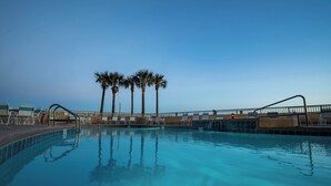 A clear blue pool with lounge chairs and palm trees in the background.