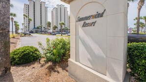 A sign for Sawmood Resort with a view of tall buildings and palm trees in the background.