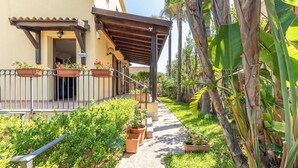 A covered outdoor area with a concrete pathway, potted plants, and a building entrance.