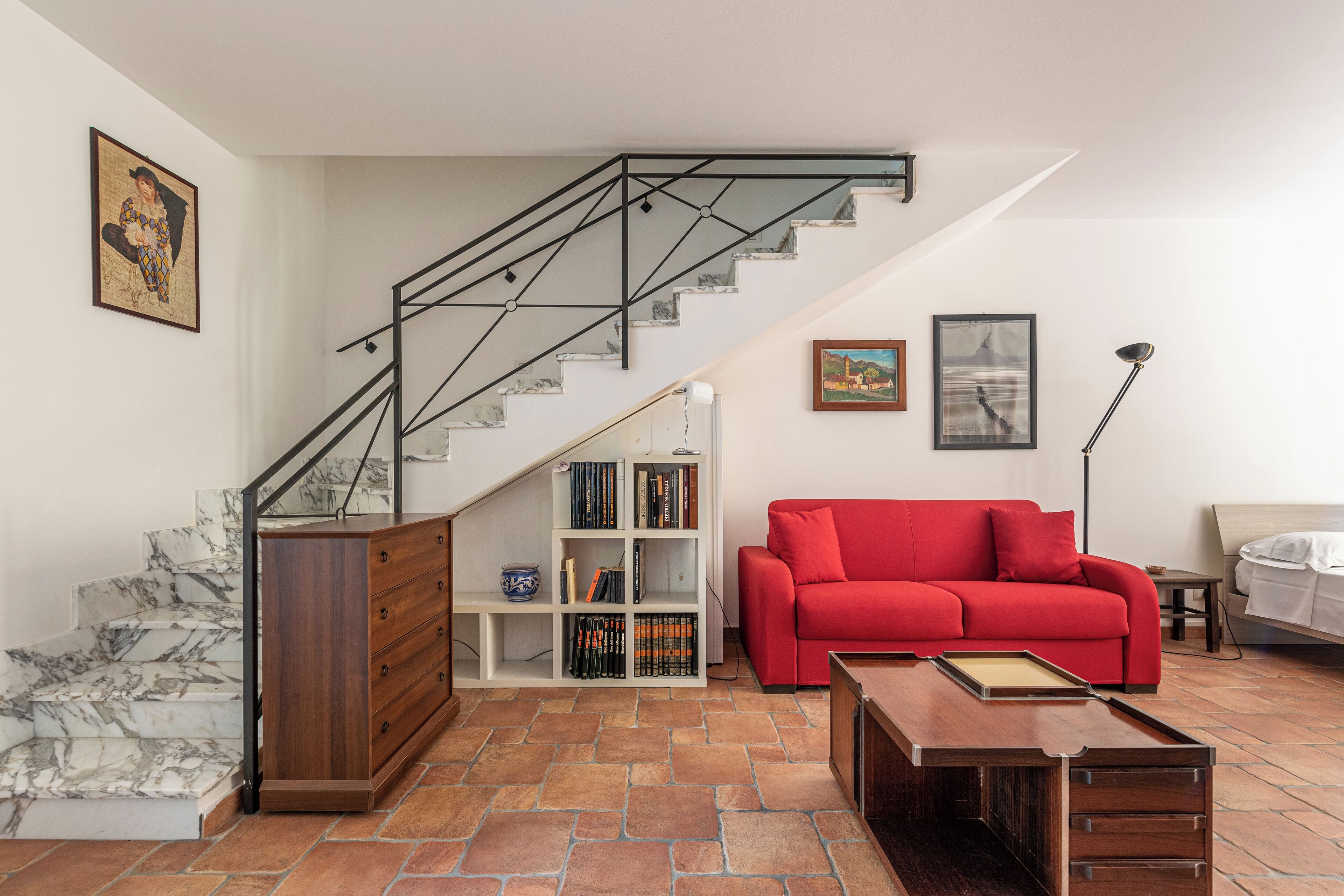 A living room with a staircase, a red sofa, a wooden cabinet, and a bookshelf.