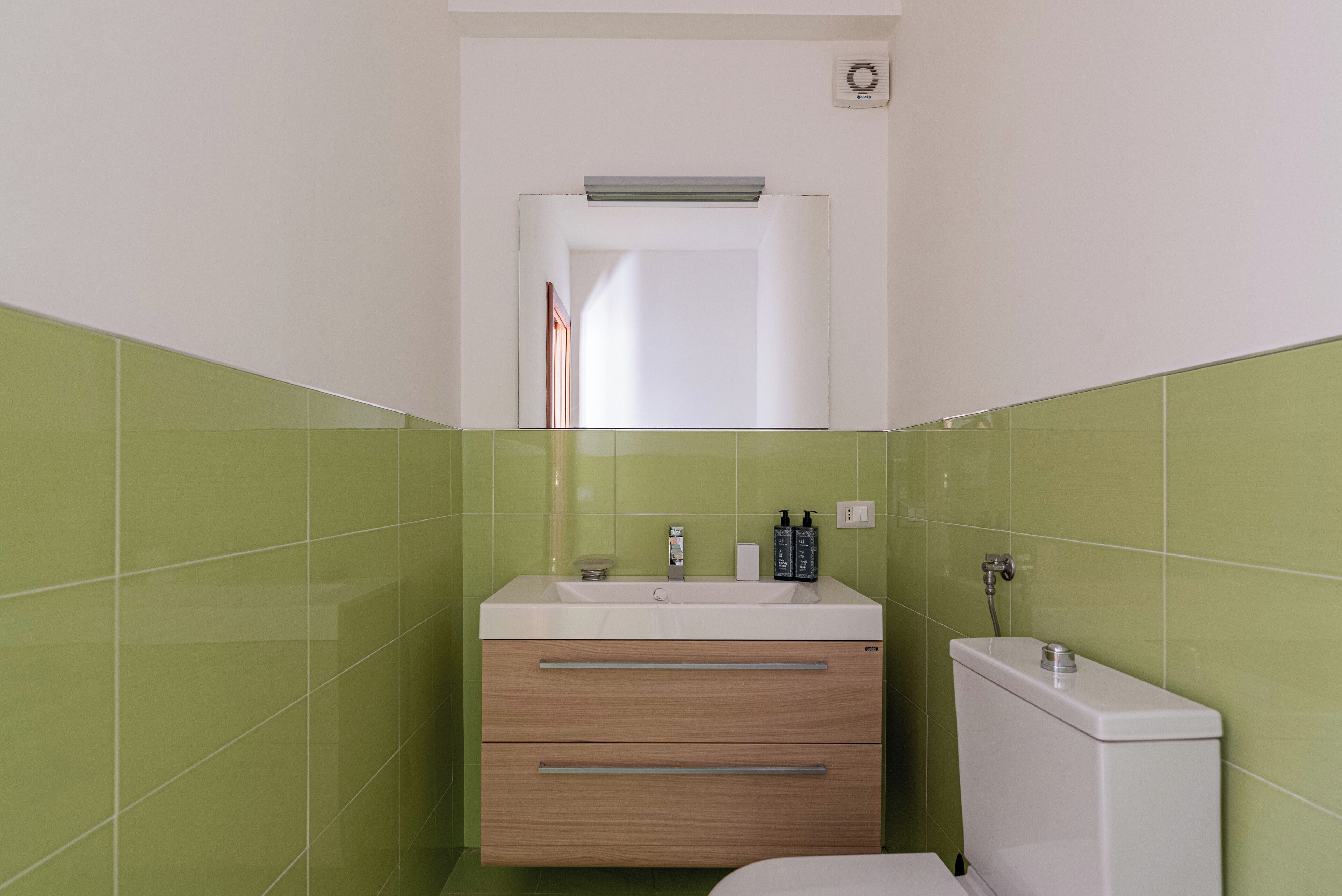 Un bagno con lavandino bianco, due cassetti, uno specchio e il water.