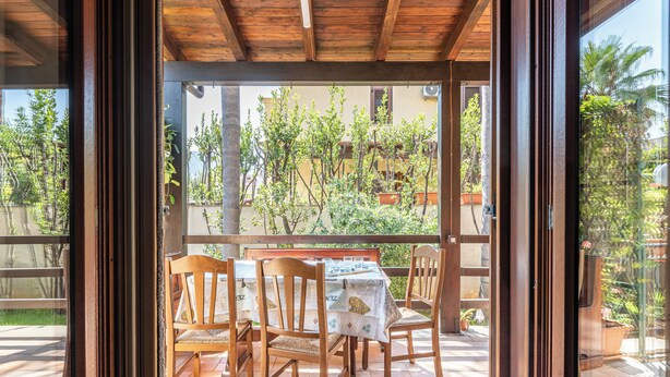 An outdoor patio with wooden chairs and a table, surrounded by a wooden pergola and potted plants.