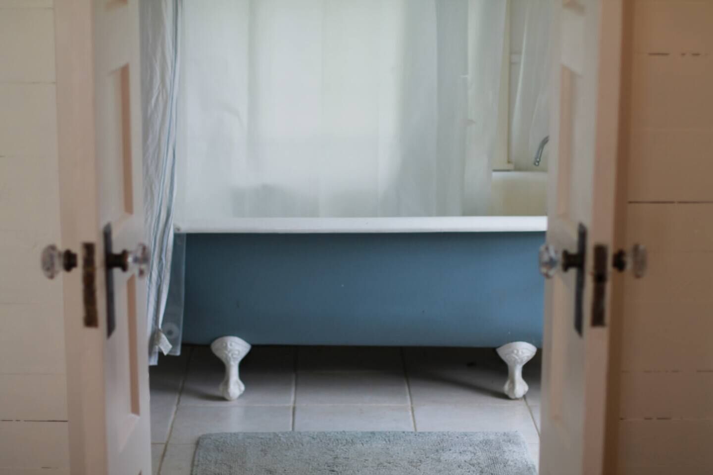A bathroom with a bathtub, a shower curtain, and a small rug on the floor.
