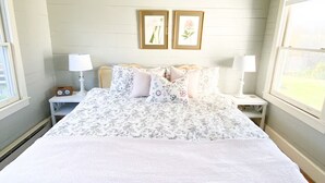A bedroom with a large bed, two bedside tables with lamps, a window with a view, and two framed pictures on the wall. - Cozy Cottage Perfect for a Charming Charlottesville (Charlottesville)