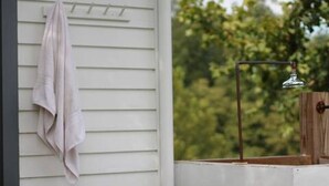 A white building with a towel hanging on a rack, a window with a metal frame, and a wooden door. - Cozy Cottage Perfect for a Charming Charlottesville (Charlottesville)