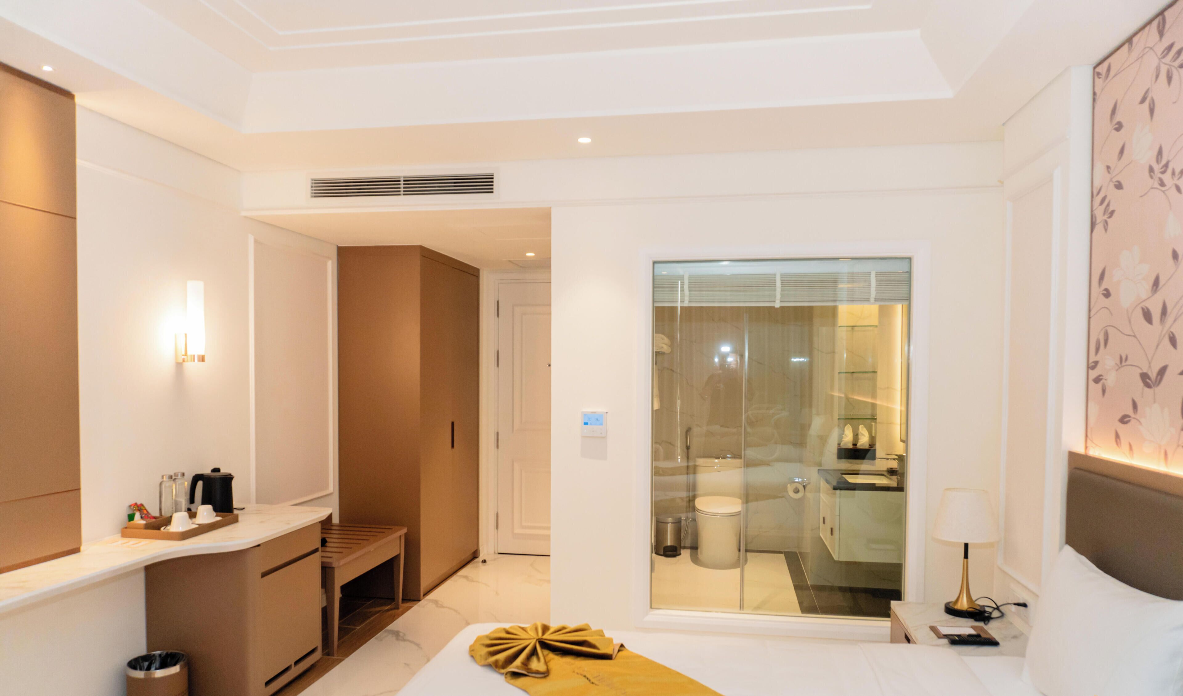 A modern hotel room with a bed, bedside table, lamp, and a view of the bathroom through a glass door.