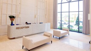 A reception area with a marble counter, two sofas, a chandelier, and large windows.