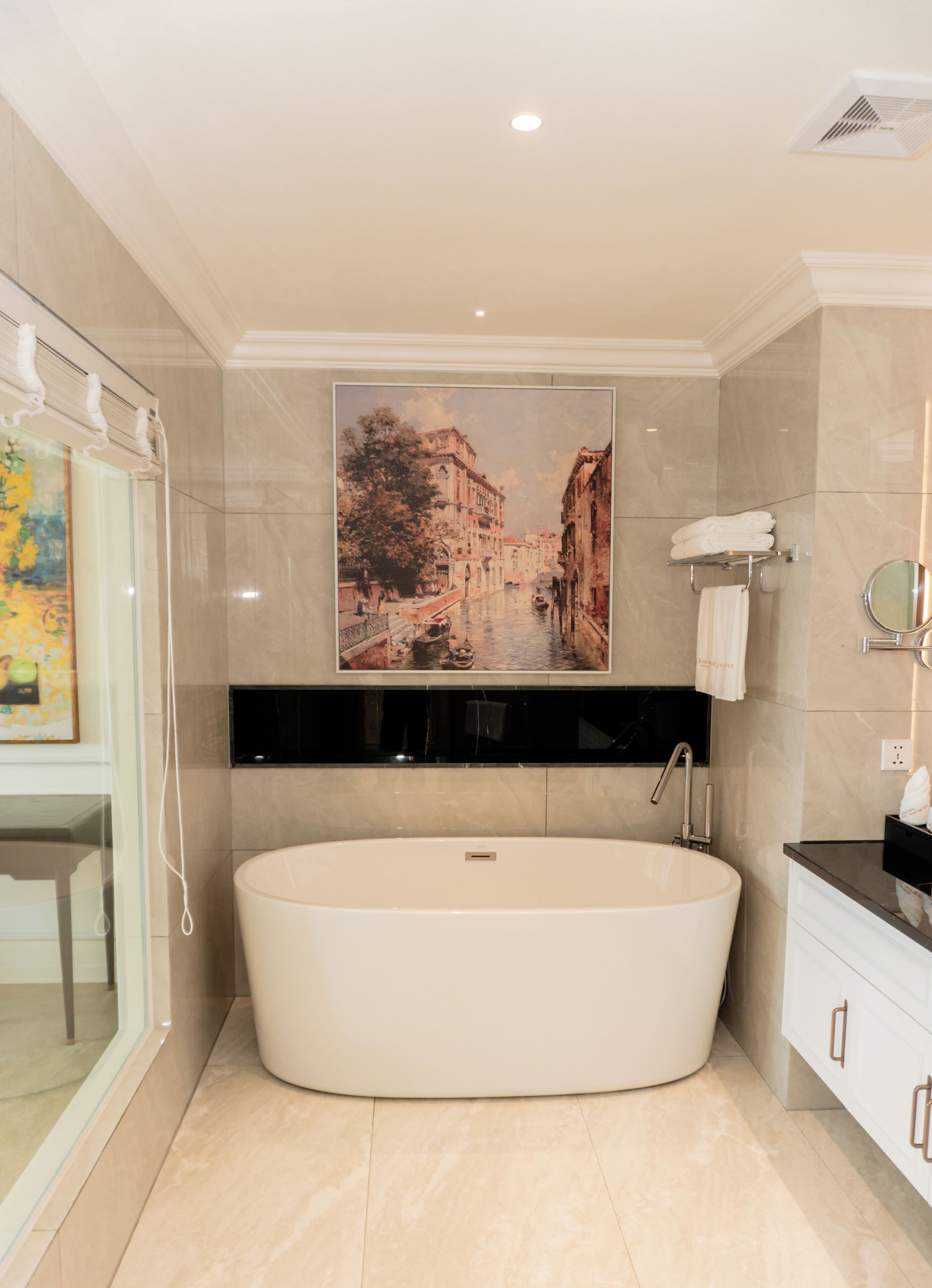 A modern bathroom with a freestanding bathtub, a large framed cityscape painting, and a glass shower enclosure.