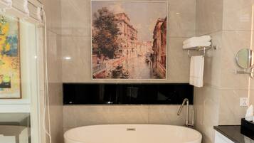 A modern bathroom with a freestanding bathtub, a large framed cityscape painting, and a glass shower enclosure.