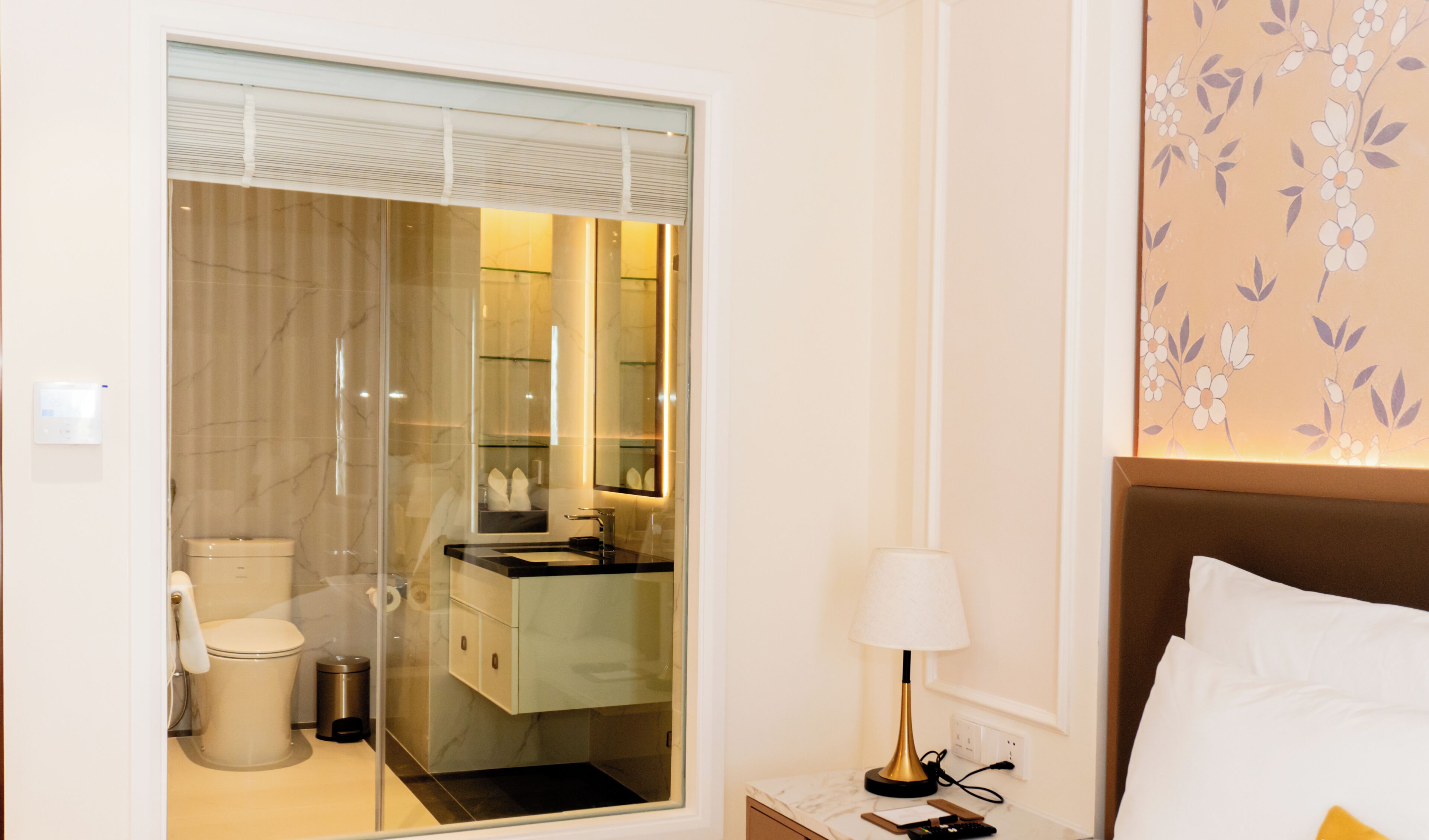 Una habitación de hotel con baño, una cama, una mesita de noche y una lámpara.