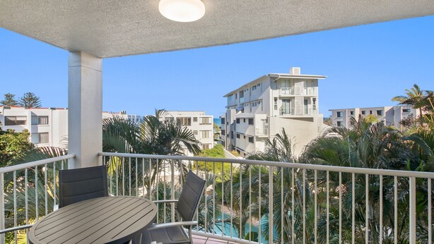 Un balcon avec une table et des chaises, donnant sur une piscine et des immeubles.