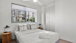 Une chambre à coucher avec un lit, deux tables de chevet, une fenêtre donnant sur un beau paysage et une armoire.