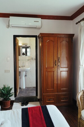 A bedroom with a bed, a wardrobe, a potted plant, a bathroom with a sink and mirror, and an air conditioning unit. - Eco Home Kathmandu Hotel (Nagarjun)