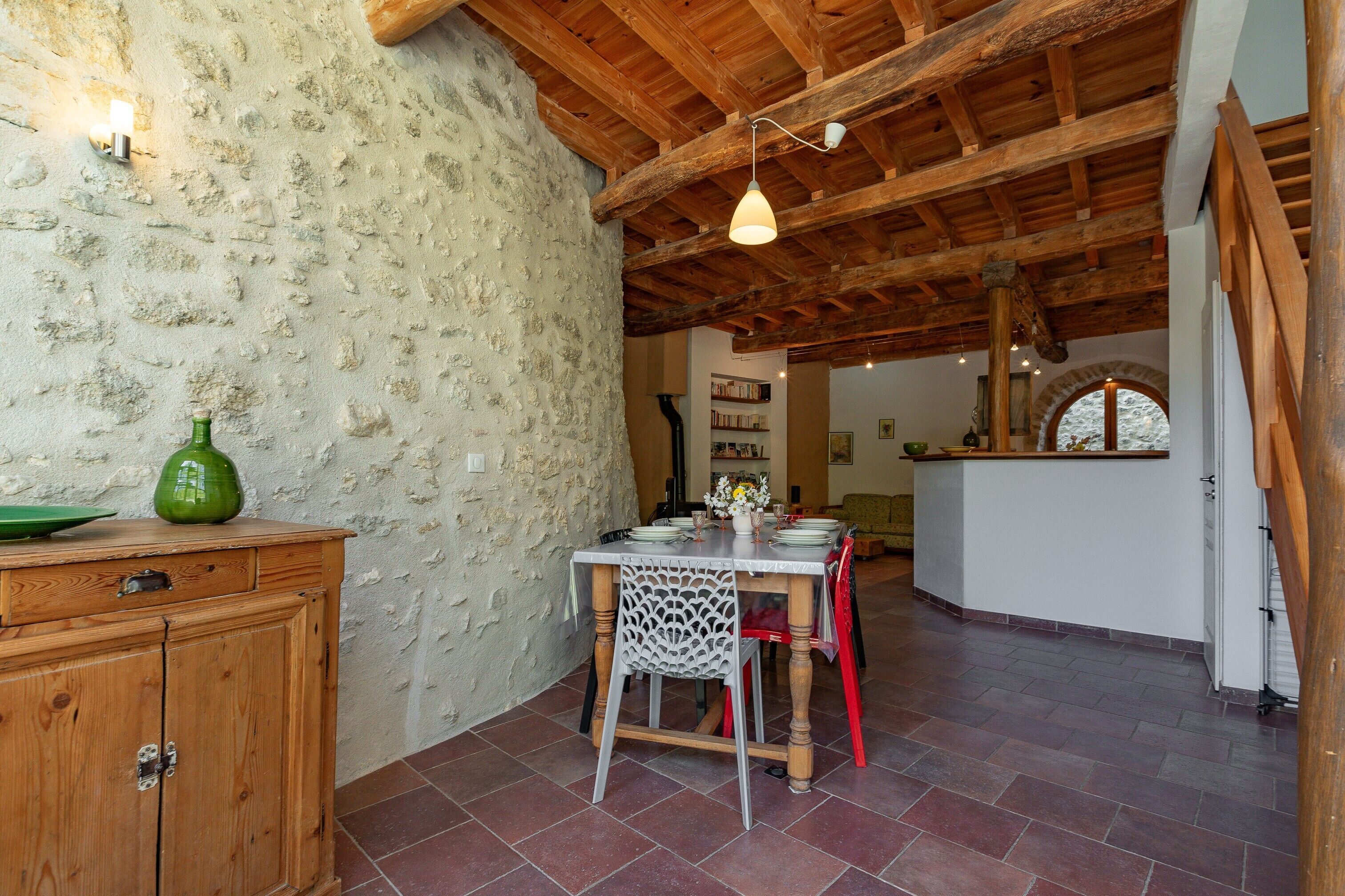 Un comedor rústico con una mesa de madera, sillas y una pared de piedra.