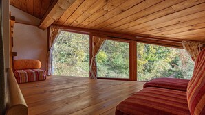 A wooden cabin interior with a large window, a wooden floor, and a red-striped sofa.