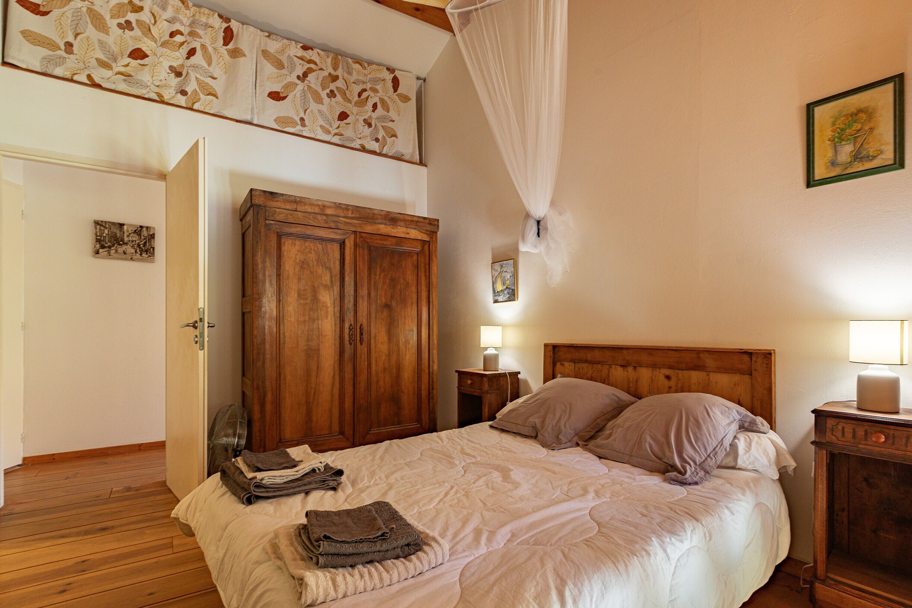 A bedroom with a bed, wooden wardrobe, bedside table, and a wall-mounted lamp.