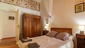 A bedroom with a bed, wooden wardrobe, bedside table, and a wall-mounted lamp.