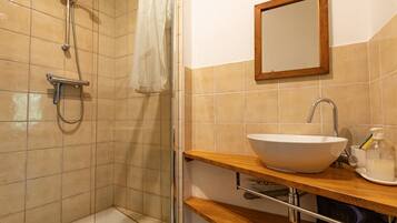 Un baño con ducha, lavamanos, espejo y estante con artículos de aseo.