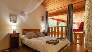 A wooden-framed bedroom with a bed, bedside tables, and a view of the outdoors.