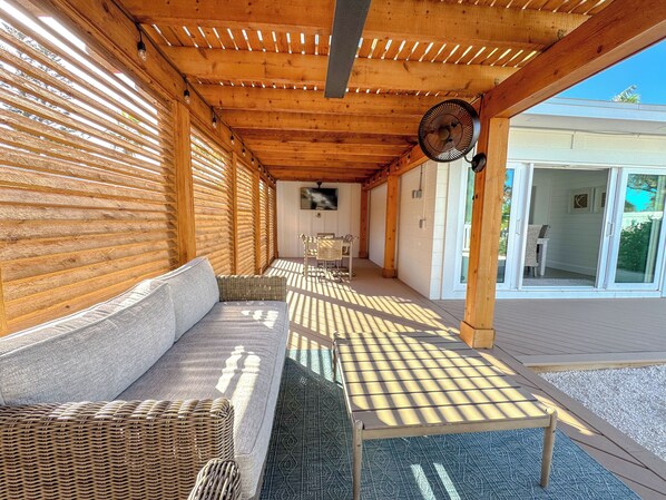 A covered outdoor seating area with a sofa and tables, wooden beams, and a fan.
