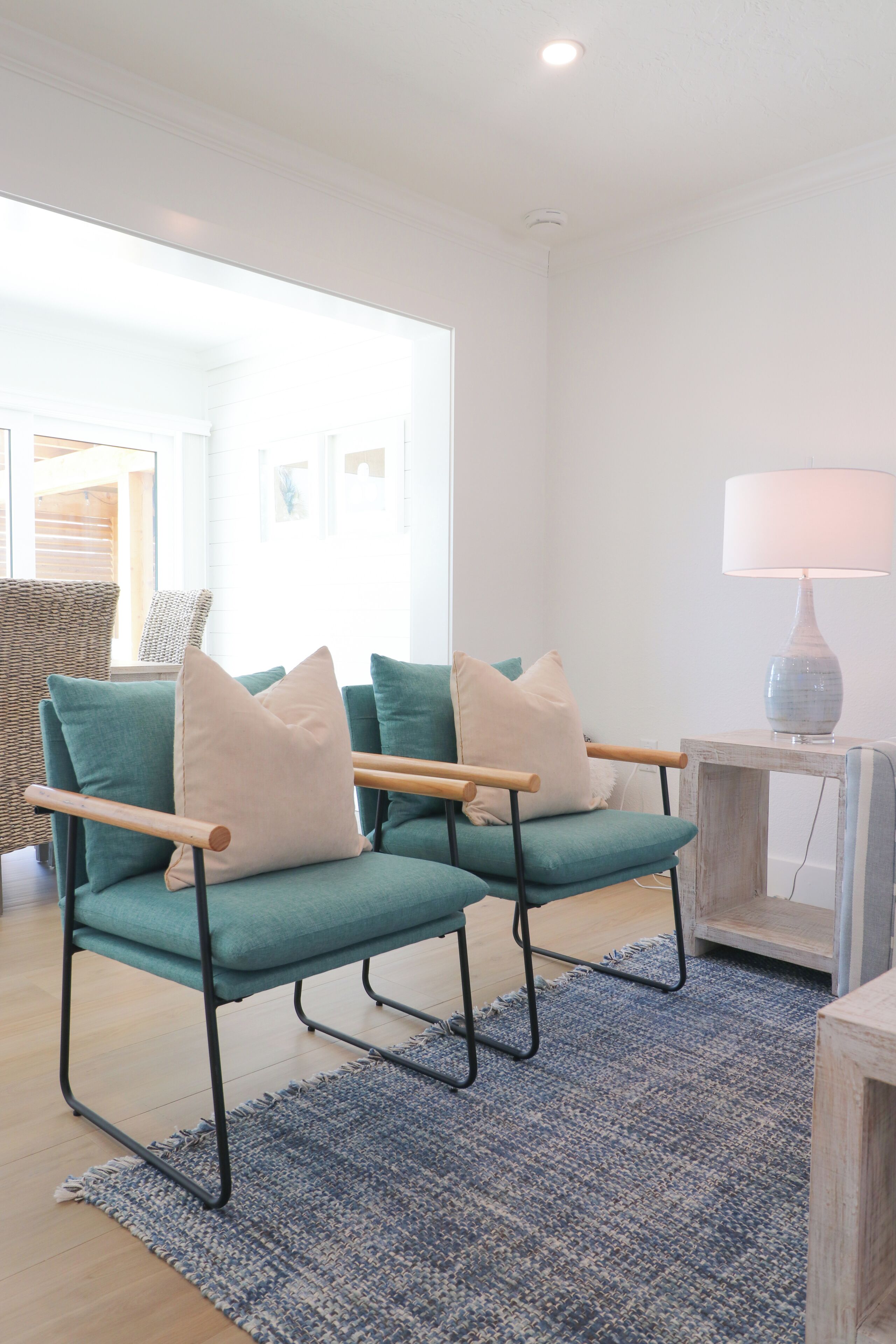 Ein modernes Wohnzimmer mit Türkis-Armstühlen, einem blauen Teppich und einem kleinen Beistelltisch mit einer Lampe.