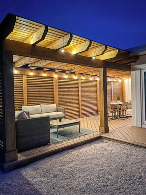 An outdoor patio with a wooden pergola, seating area, and a dining table.
