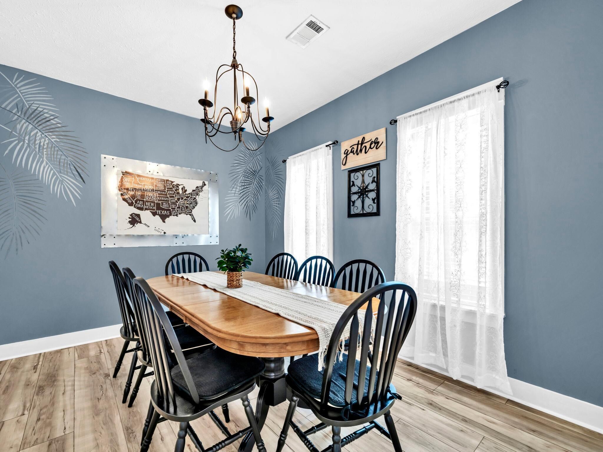 A dining room with a wooden table, black chairs, a chandelier, a map of the USA on the wall, and a 'family' sign.