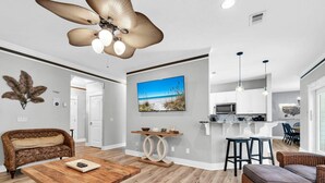 A modern living room with a wooden coffee table, a large ceiling fan, and a television mounted on the wall. - Sea the Blessings (Panama City Beach)