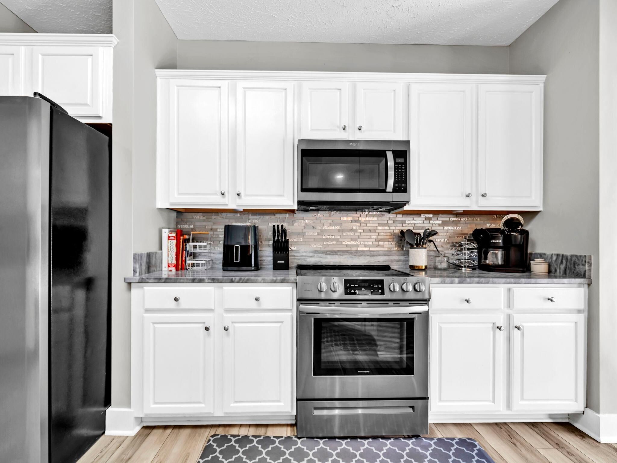 A modern kitchen with white cabinets, a stainless steel refrigerator, a microwave, a coffee maker, and an oven.
