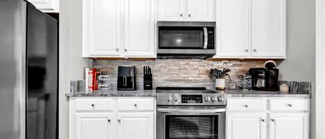 A modern kitchen with white cabinets, a stainless steel refrigerator, a microwave, a coffee maker, and an oven.