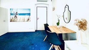 A room with a blue carpet, a wooden table with chairs, a white cabinet, a door, and a wall-mounted mirror. - Comfy Room Shared Apt, 13-min to Belvedere Palace (Vienna)