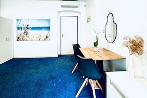 Quarto com carpete azul, mesa de madeira com cadeiras, armário branco, porta e espelho fixado na parede.