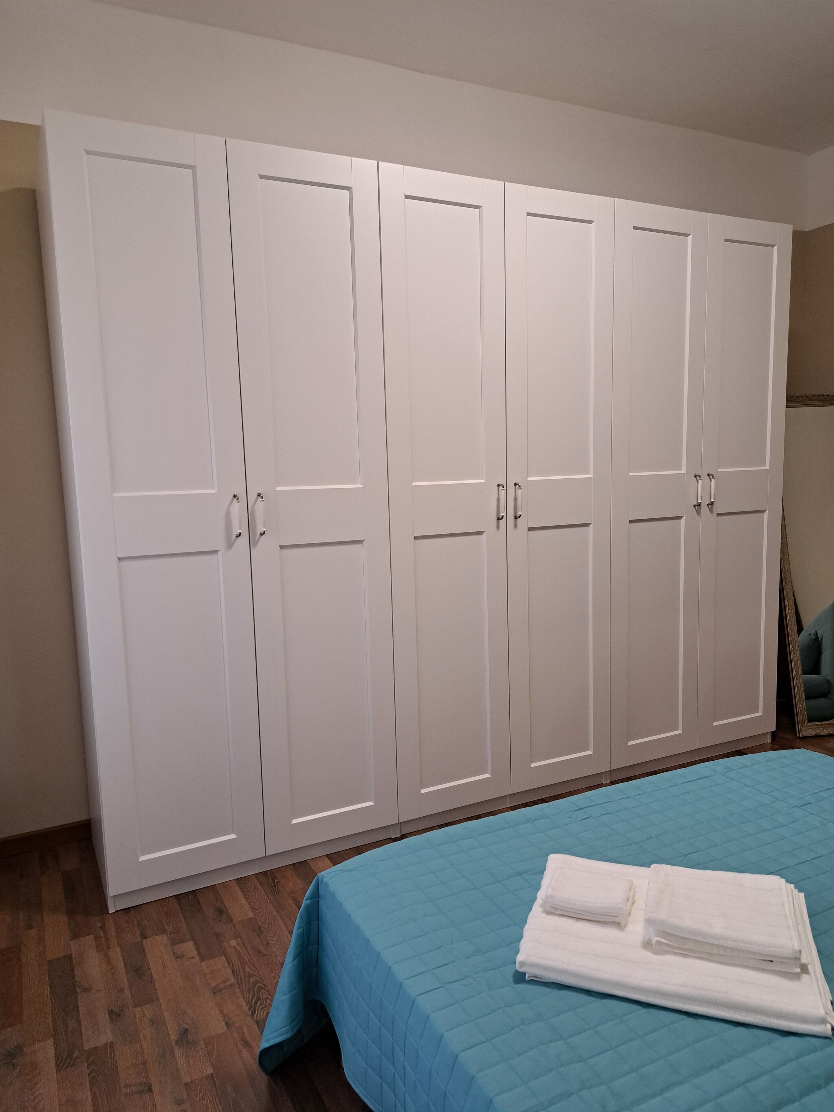 Een slaapkamer met een grote garderobe, een bed met een blauwe spreideken en een houten vloer.