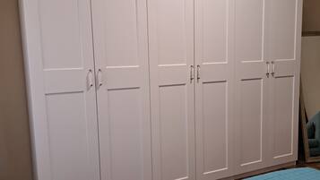 Een slaapkamer met een grote garderobe, een bed met een blauwe spreideken en een houten vloer.