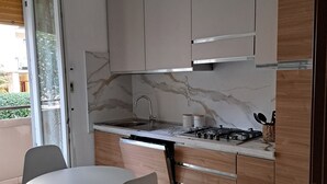 A modern kitchen with a round dining table and chairs, a built-in stove, and a sliding door leading to a balcony. - FAMILY APARTMENT VERY CLOSE TO SAN GIULIANO HOSPITAL (Novara)