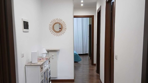 A hallway with wooden flooring, white walls, and a sunburst mirror. There is a small cabinet with a coffee maker and a picture frame on the left. - FAMILY APARTMENT VERY CLOSE TO SAN GIULIANO HOSPITAL (Novara)