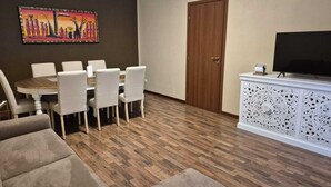 A dining area with a round table and chairs, a painting on the wall, a wooden door, and a white cabinet with a TV. - FAMILY APARTMENT VERY CLOSE TO SAN GIULIANO HOSPITAL (Novara)