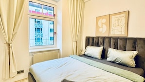 Un dormitorio con cama, cortinas, radiador, ventana y una obra de arte en la pared.