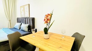 Una habitación con una cama, un sofá, una mesa de comedor con sillas, un jarrón con flores y dos copas de vino.