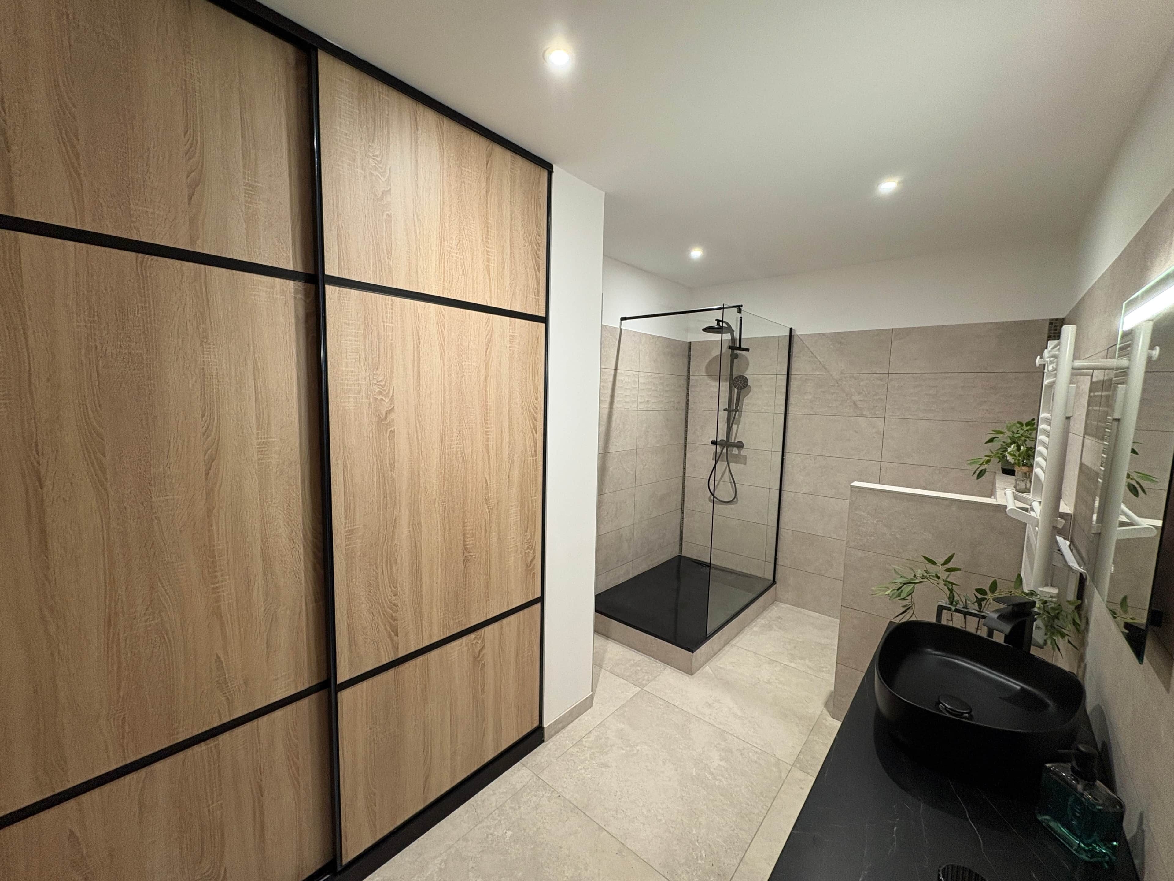 A modern bathroom with a walk-in shower, a black bathtub, and a wooden panel wall.