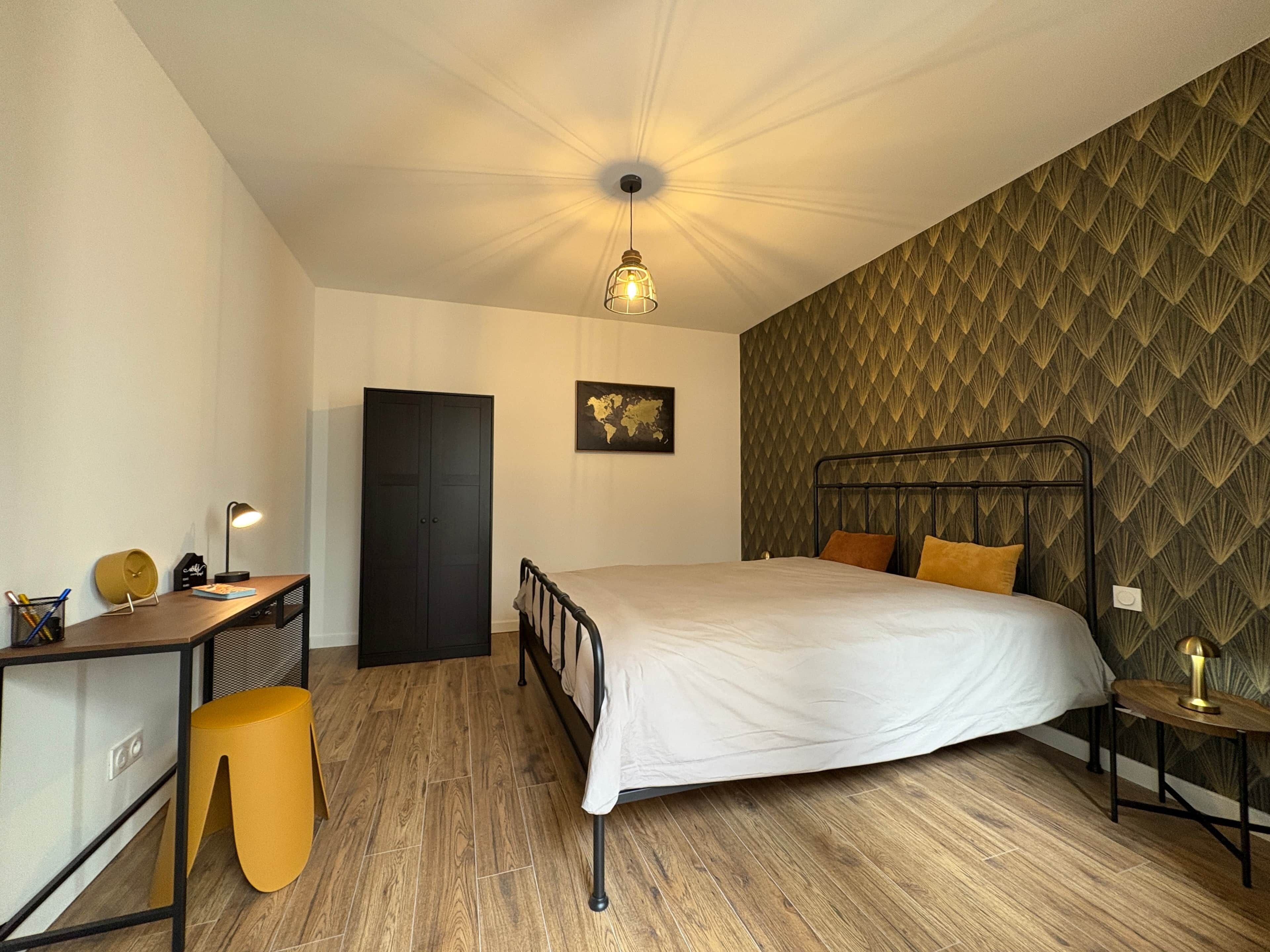 Une chambre à coucher comprenant un lit, un bureau, une chaise, une armoire et un mur décoré d’un motif.