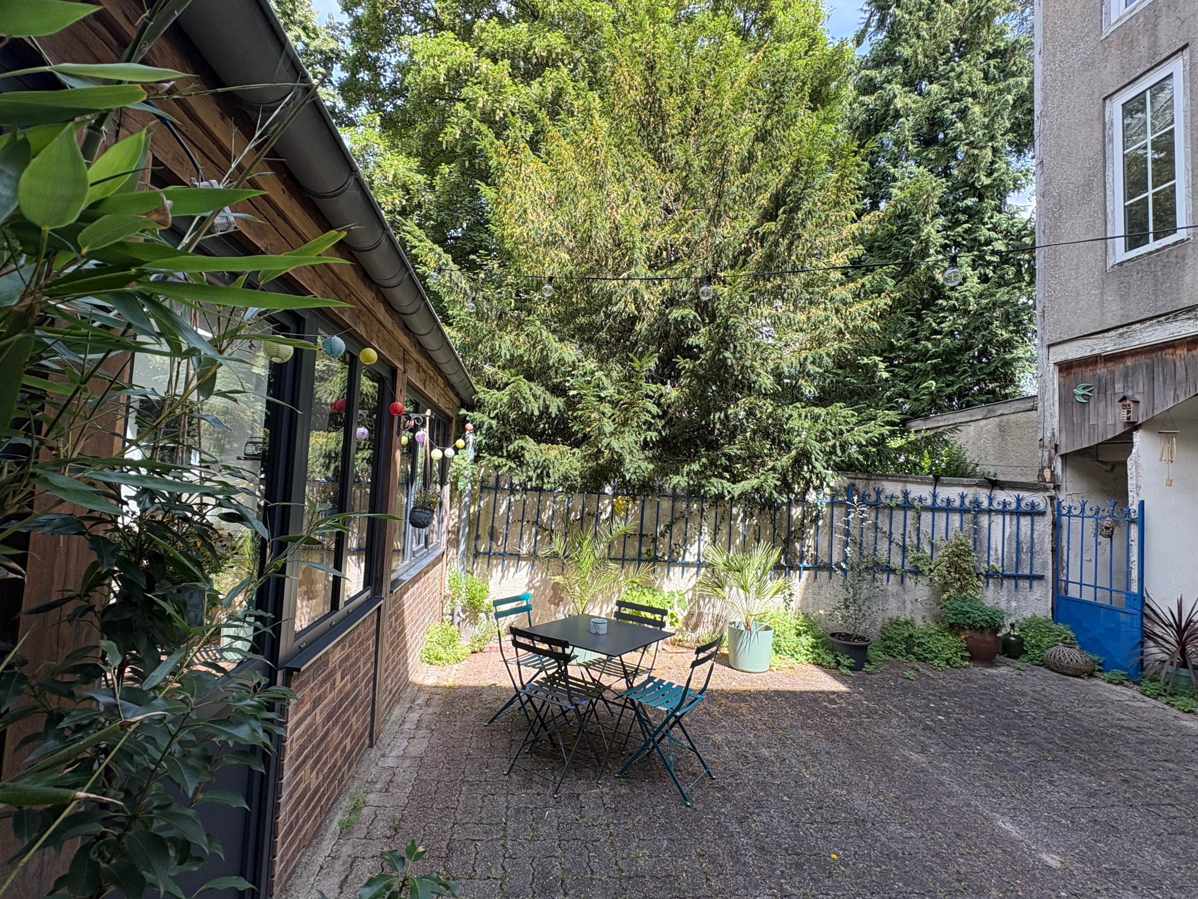 Eine Terrasse mit Tisch und Stühlen, umgeben von Topfpflanzen und einer Backsteinmauer.