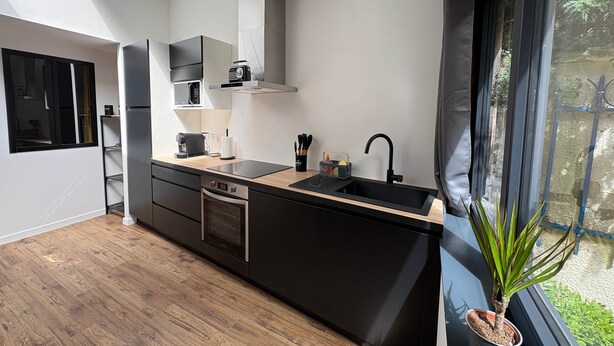 Une cuisine moderne dotée d’un plan de travail noir, d’appareils électroménagers en acier inoxydable et d’une fenêtre donnant sur un paysage verdoyant.